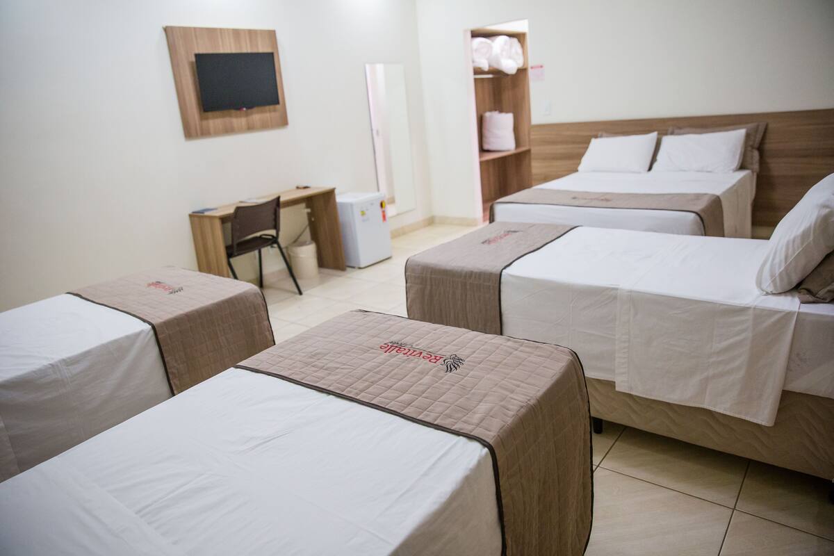 Ein Hotelzimmer mit drei Einzelbetten, einem Schreibtisch, einem Stuhl und einem Kleiderschrank.