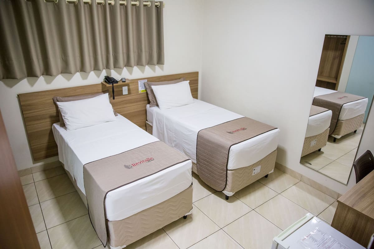 Ein Hotelzimmer mit zwei Einzelbetten, einem Holzkopfende, einem Nachttisch mit Telefon und einem Spiegel.