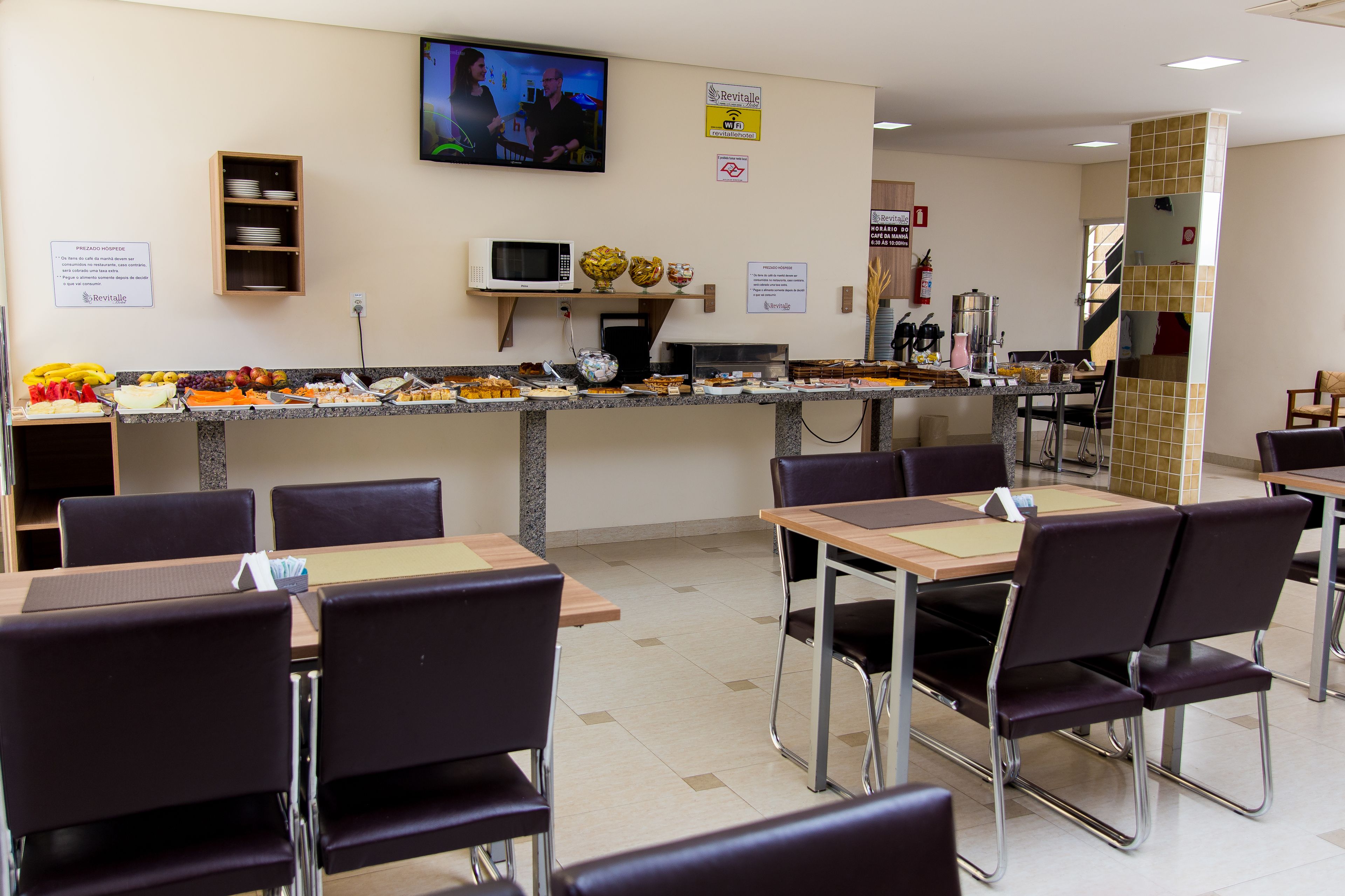 Eine Cafeteria mit Buffet, Tischen, Stühlen und einem Fernsehbildschirm.