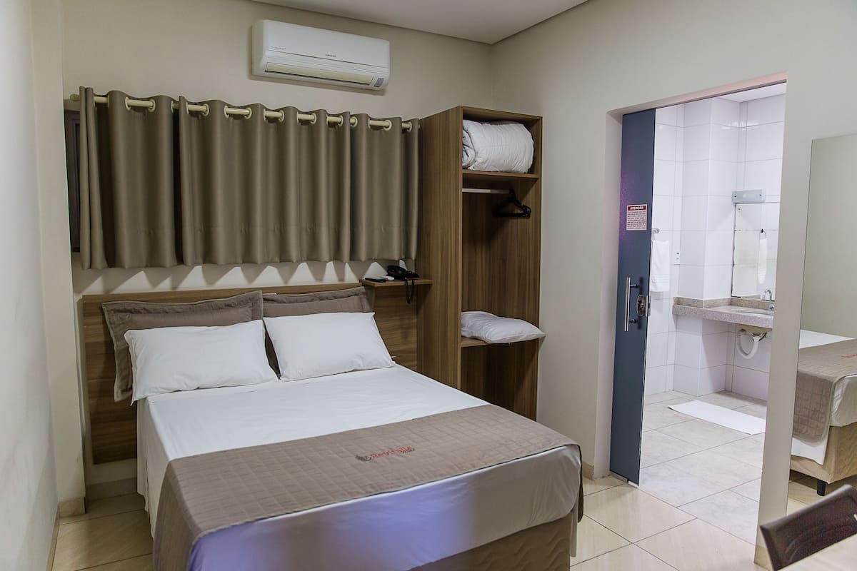 Ein Hotelzimmer mit Bett, Kleiderschrank, Bad mit Waschbecken und Spiegel sowie einer Duschkabine.