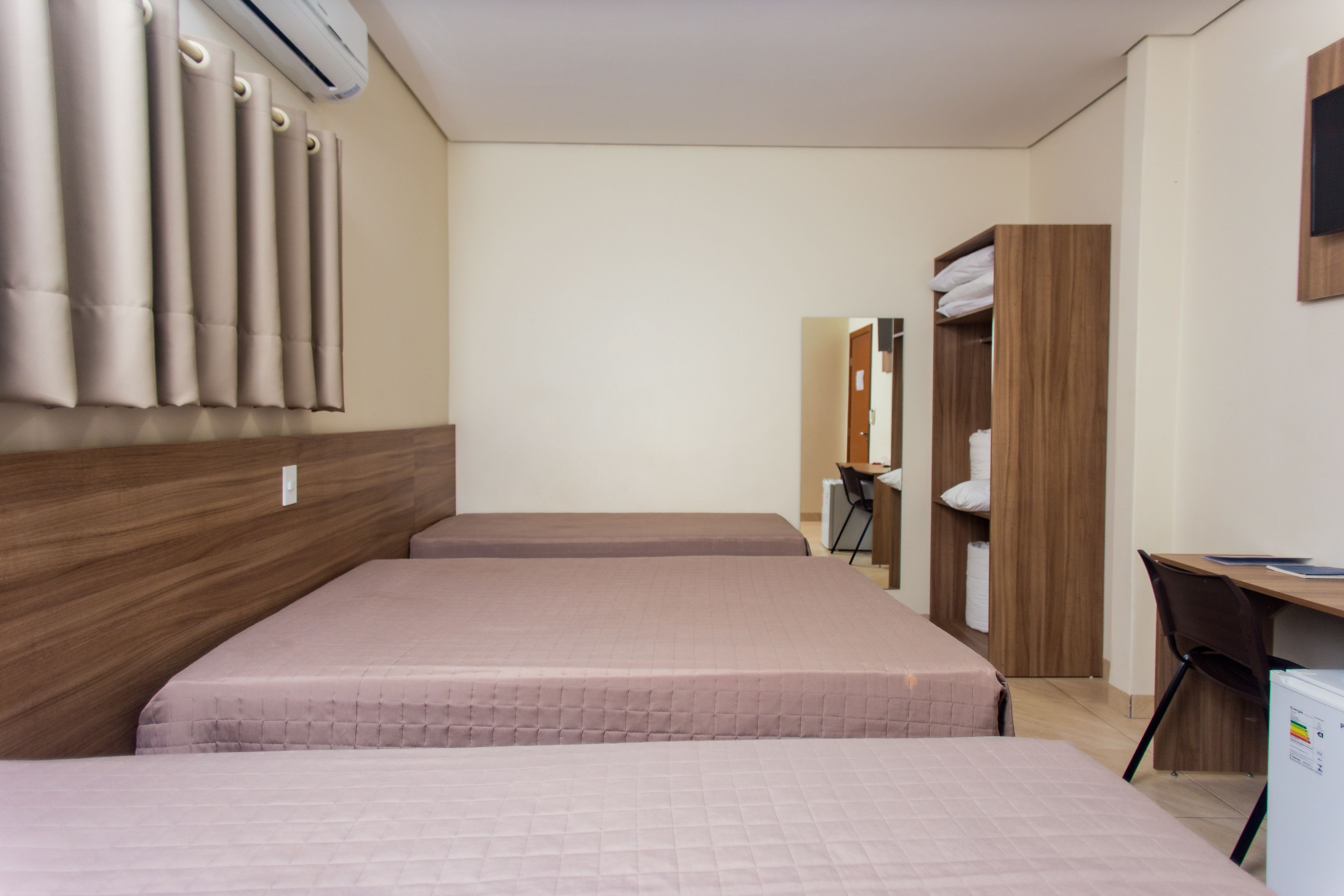 A hotel room with two beds, a desk, a chair, and a wardrobe.