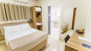 Una habitación de hotel con cama, escritorio, silla, espejo, baño y estante con toallas.