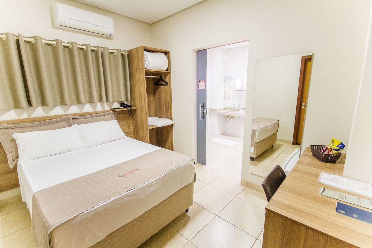 Ein Hotelzimmer mit Bett, Schreibtisch, Stuhl, Spiegel, Bad und einem Regal mit Handtüchern.