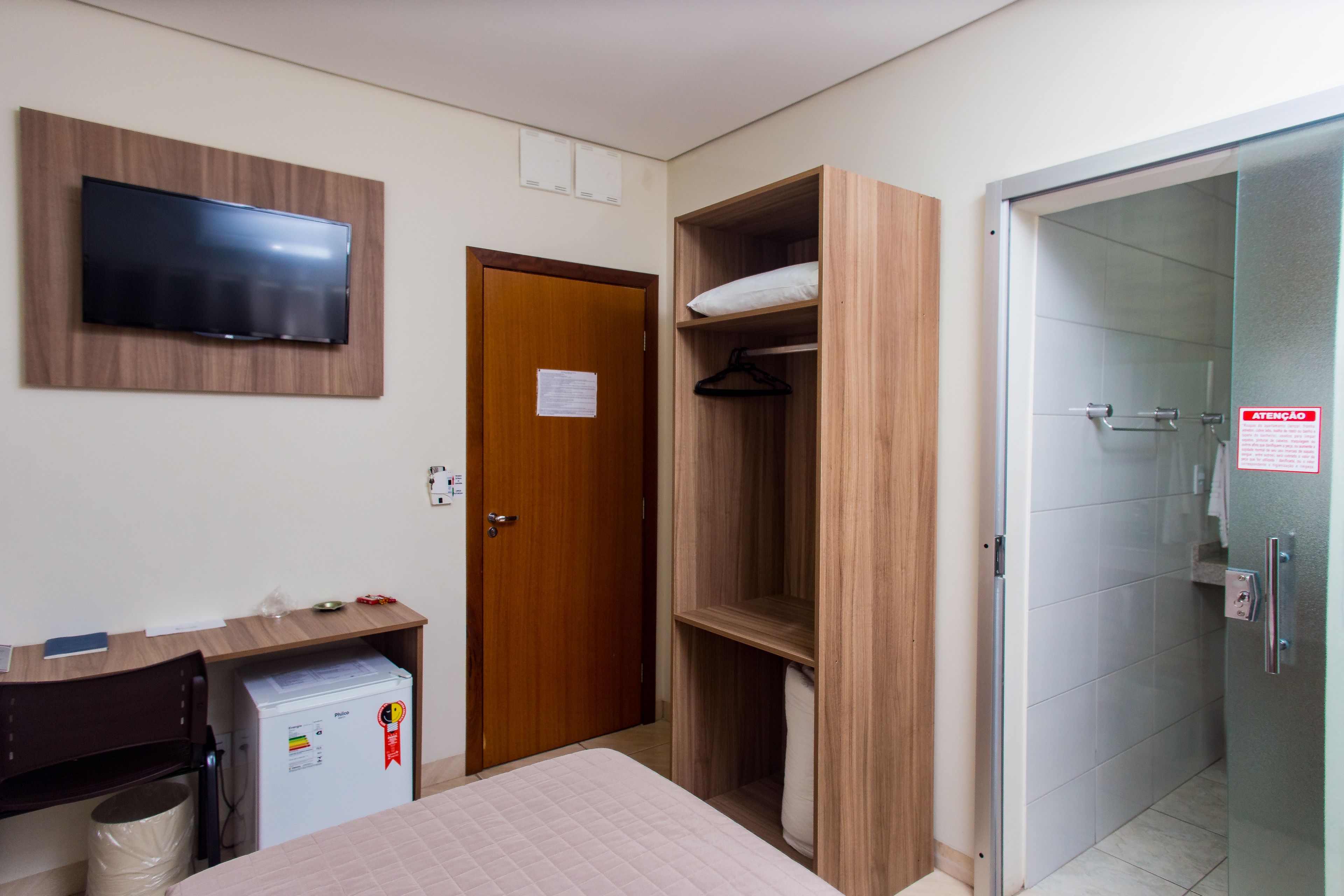 Een hotelkamer met een bed, een bureau met een computer, een aan de muur bevestigde televisie, een kledingkast en een douchehoek.