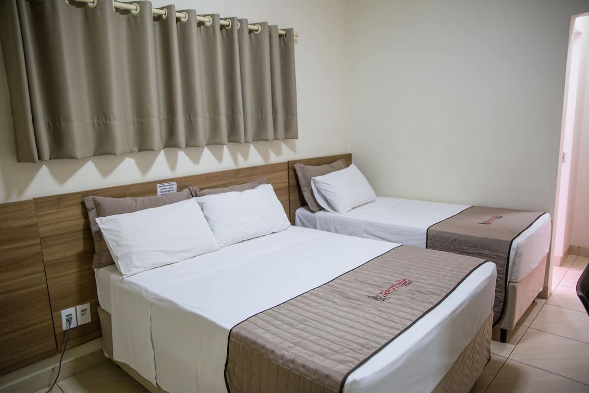 Ein Hotelzimmer mit zwei Betten, einem hölzernen Kopfteil, einem Vorhang und einem Nachttisch.