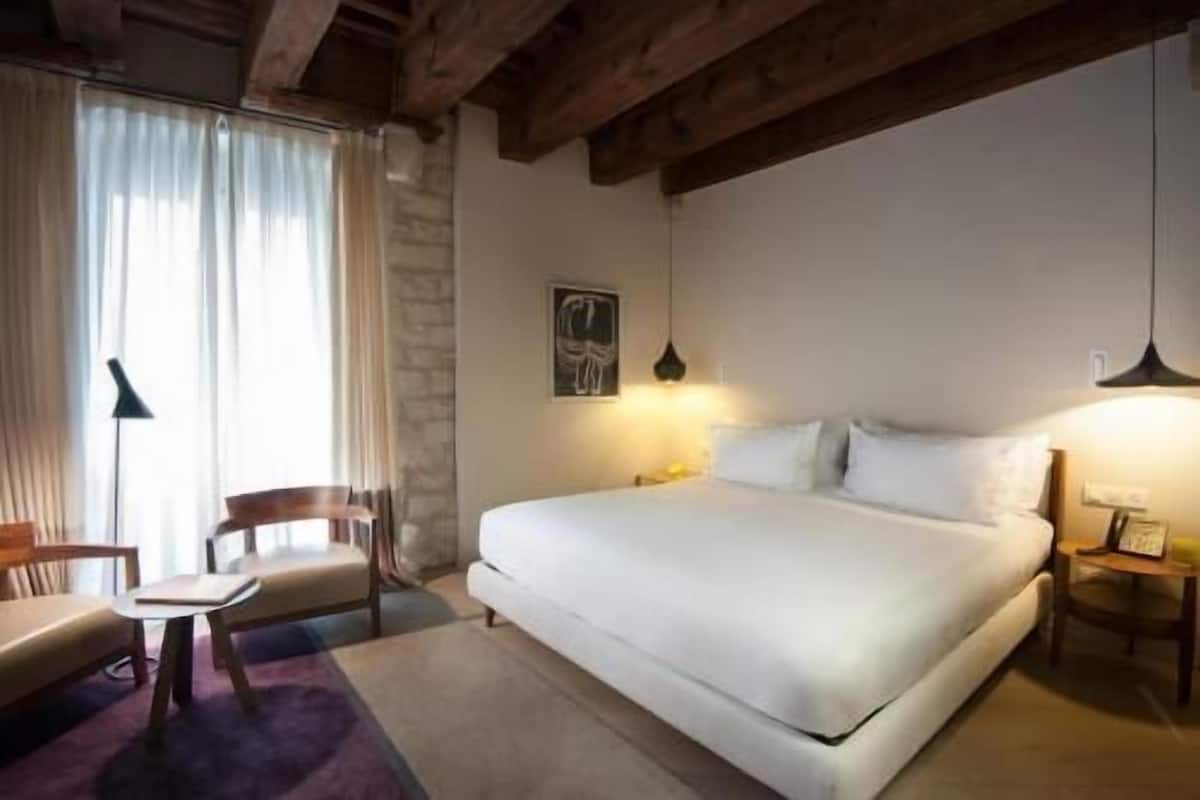 A bedroom with a bed, a chair, a desk, and a lamp.