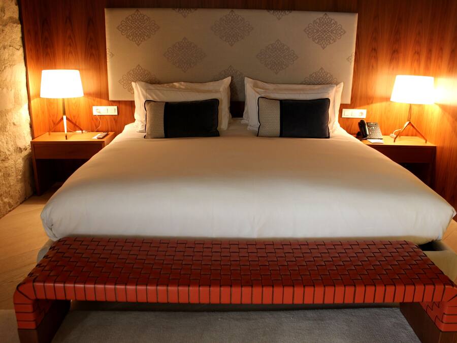 A hotel room with a large bed, two bedside lamps, a telephone, and a red bench.