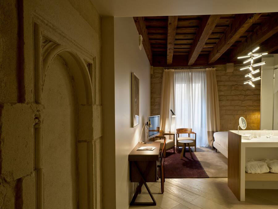 Quarto com escrivaninha de madeira, cama, banheiro e parede de pedra.