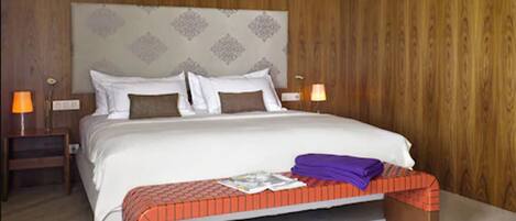 A bedroom with a large bed, wooden panel walls, two bedside tables with lamps, and a bench at the foot of the bed.