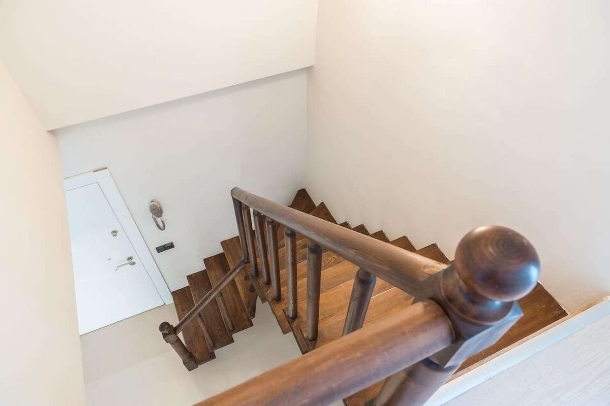 Una escalera de madera con barandilla y una puerta blanca al final.