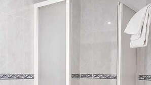 A walk-in shower with a glass door, tiled walls, and a small shelf. - Pensión Bilbao (Bilbao)