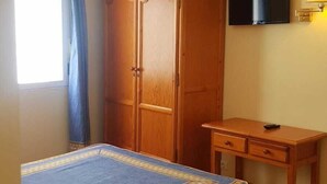 A bedroom with a bed, a wooden wardrobe, a desk, a television, and a window with curtains. - Pensión Bilbao (Bilbao)