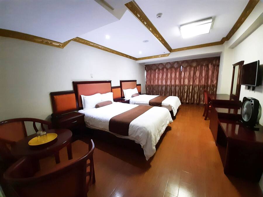 Ein Hotelzimmer mit zwei Betten, einem Schreibtisch, einem Stuhl, einem Fernseher und einem Deckenventilator.