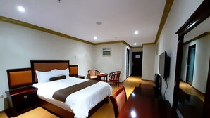 Habitación de hotel con una cama grande, un escritorio de madera, una silla, un televisor y una puerta que da a otra habitación.
