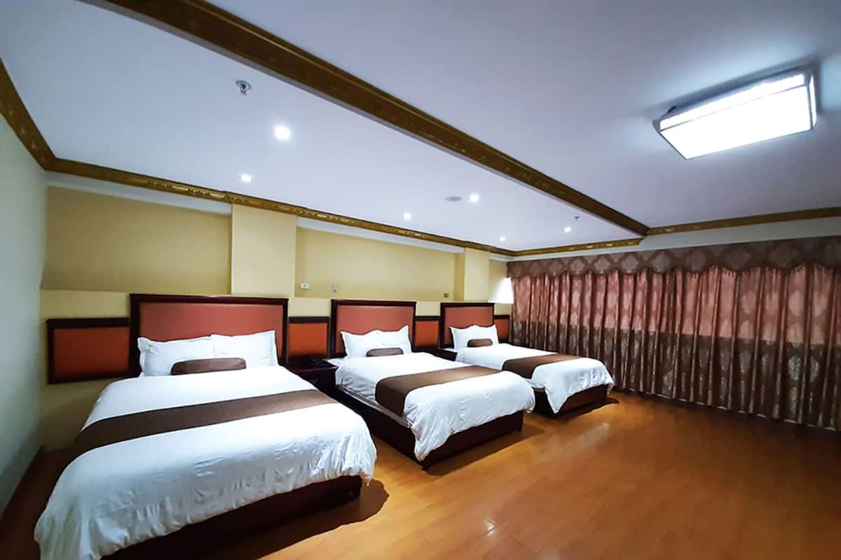 A hotel room with three beds, wooden flooring, and a large window with curtains.