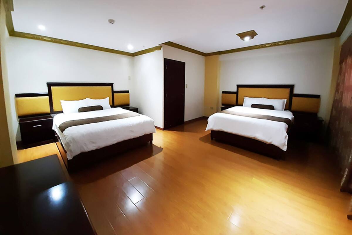 A hotel room with two beds, wooden flooring, and a dark-colored wardrobe.