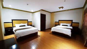 Habitación de hotel con dos camas, piso de madera y un armario de color oscuro.