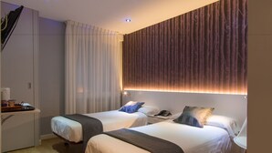Une chambre d’hôtel avec deux lits, un bureau avec une chaise et une grande fenêtre avec des rideaux.