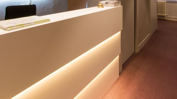 Un comptoir d’accueil avec une enseigne indiquant « TC CENTRAL », un espace d’attente avec un mur décoré de motifs, et un radiateur en arrière-plan.