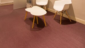Un espace d’accueil comprenant une vitrine, deux chaises blanches aux pieds en bois et un sol recouvert d’une moquette.