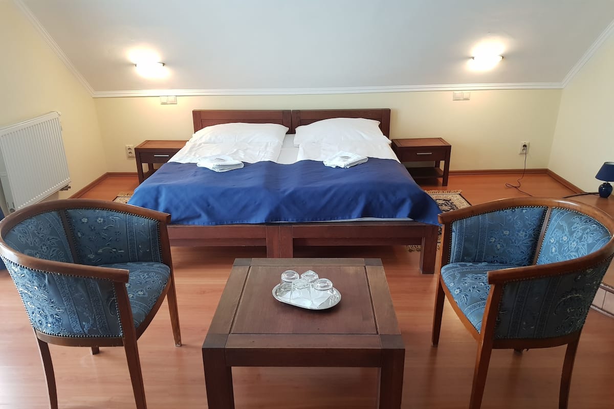 Une chambre à coucher avec un lit double, deux tables de chevet, une table en bois et deux fauteuils rembourrés.
