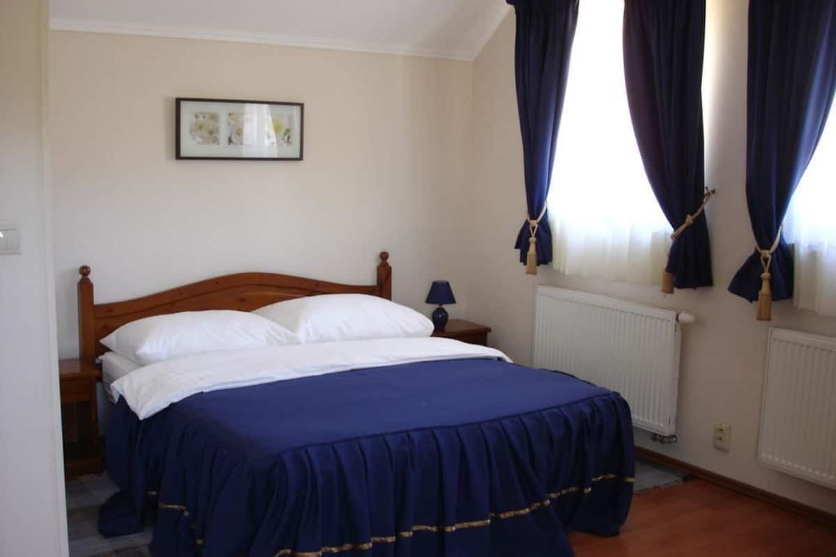 Une chambre à coucher avec un lit en bois, une table de chevet, un tableau encadré au mur et une fenêtre avec des rideaux.
