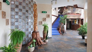 Un hall d’hôtel avec un escalier, des plantes en pot et des œuvres d’art encadrées accrochées aux murs.