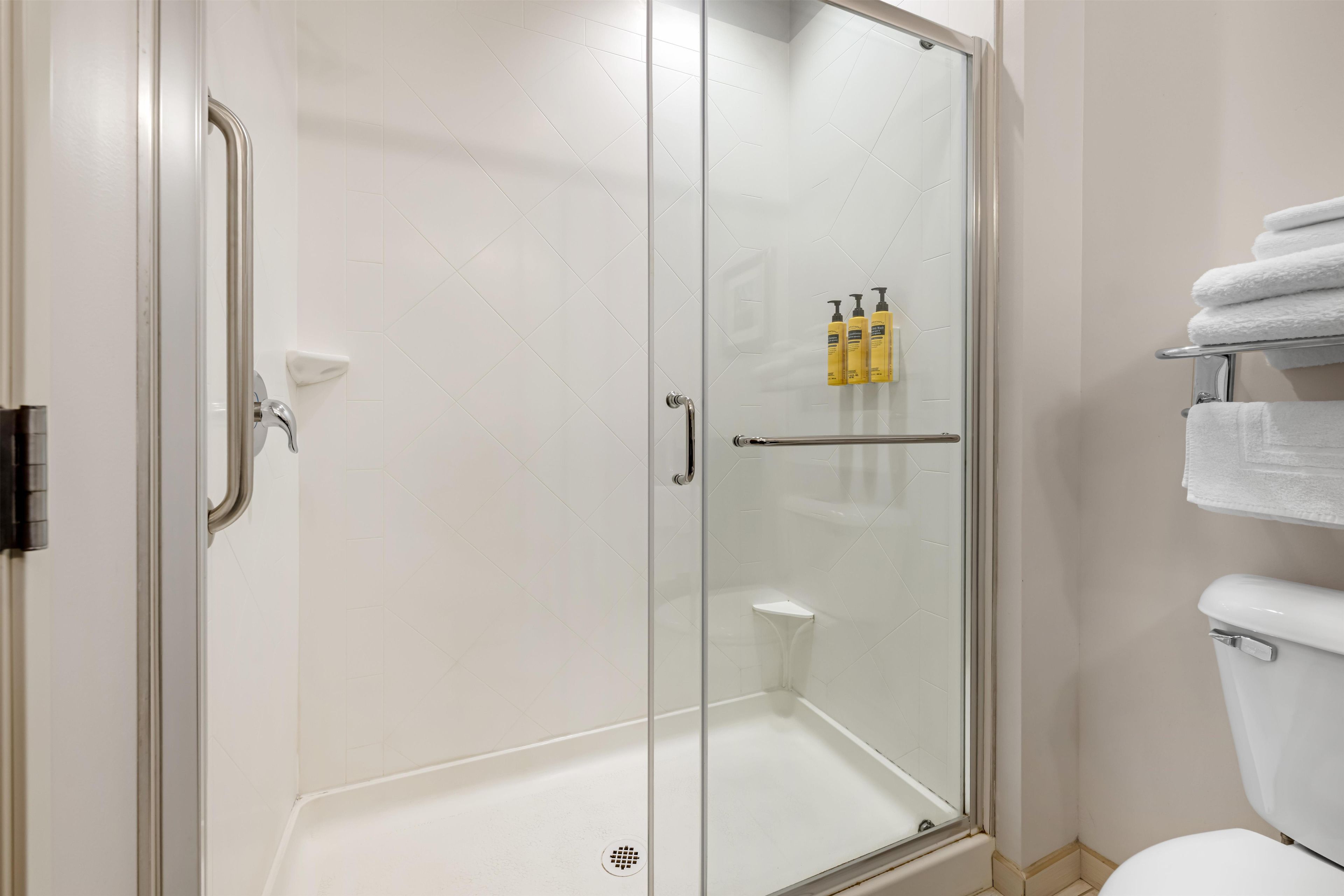 A glass-enclosed shower with a white tiled wall, a glass door, and a metal handle.