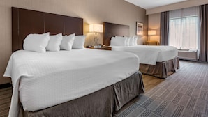 Hotellihuone, jossa on kaksi sänkyä, suuri päätyseinä, yöpöytälamput, yöpöytä ja ikkuna, jossa on verhot.