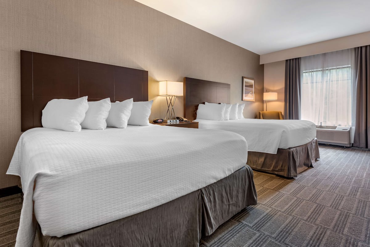 A hotel room with two beds, a large headboard, bedside lamps, a nightstand, and a window with curtains.