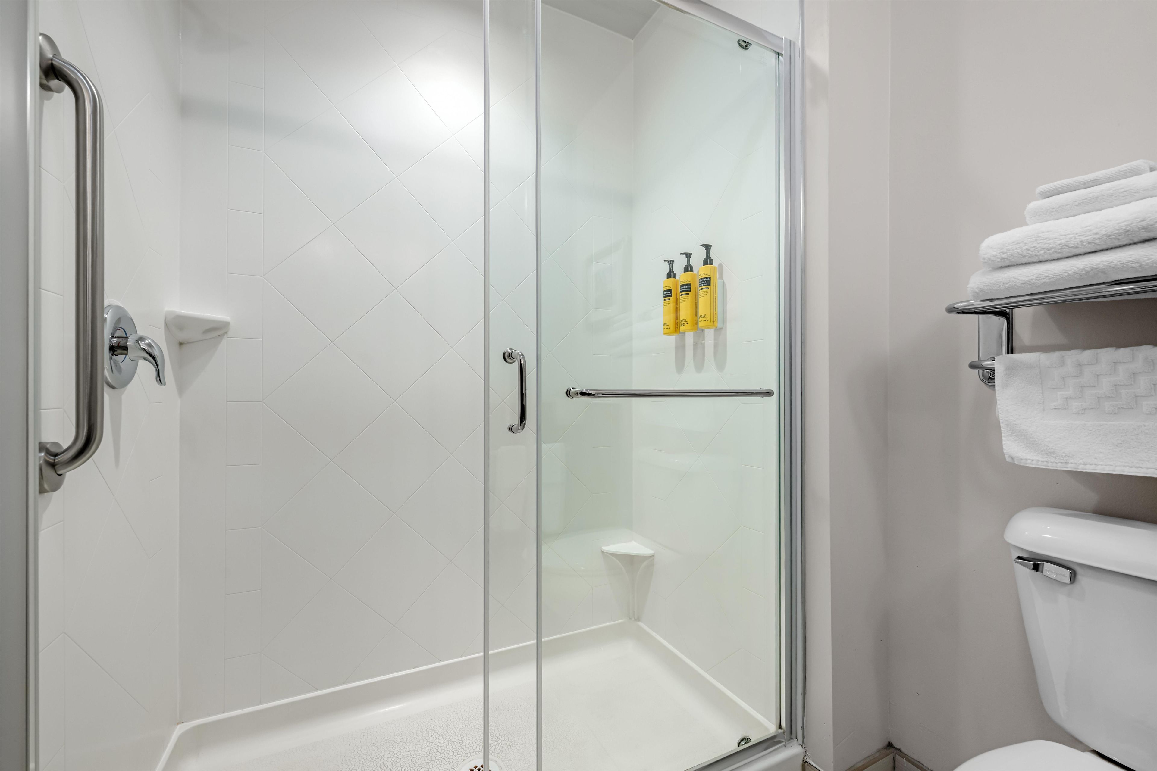A modern bathroom with a glass shower enclosure, a white toilet, and a towel rack with neatly folded towels.