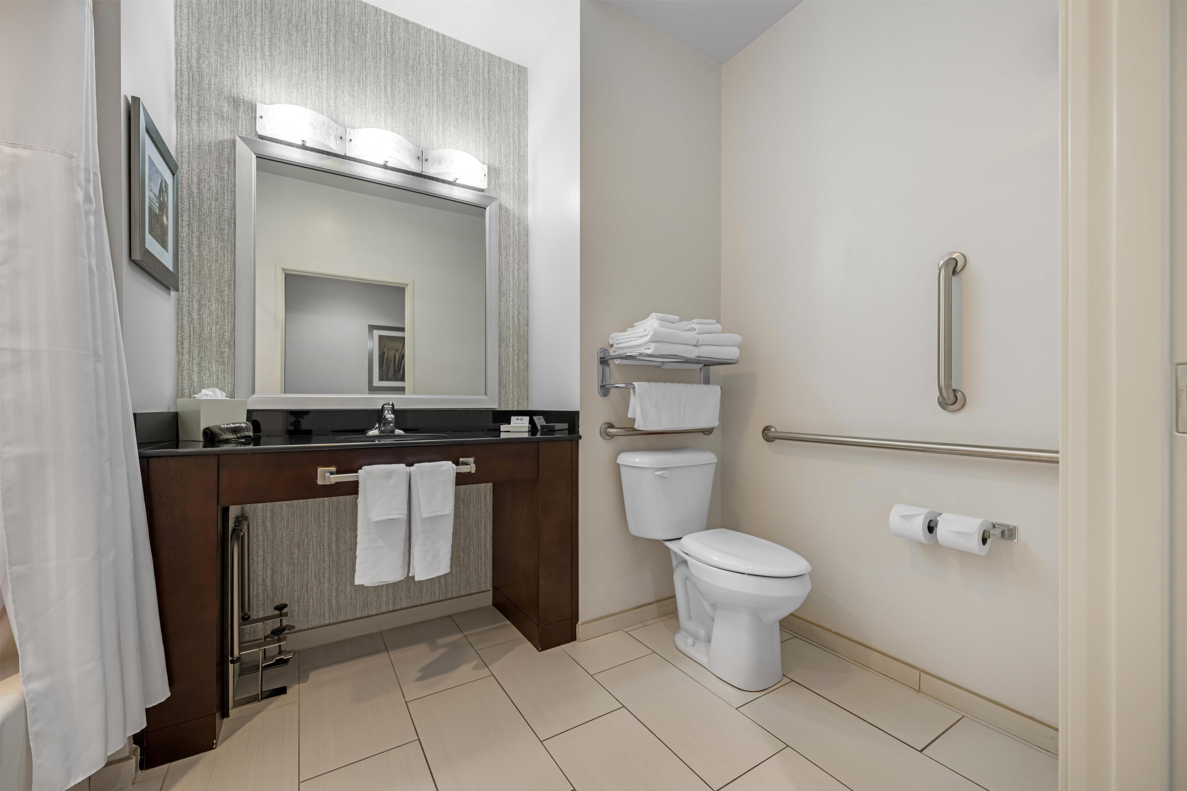 A modern bathroom with a vanity, toilet, and handrail.