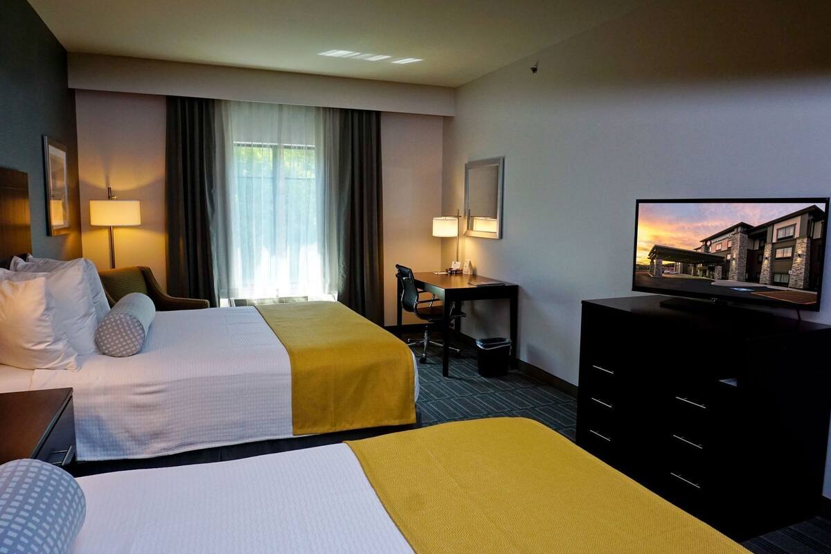 A hotel room with two beds, a desk, a television, and a window with curtains.