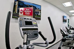 Een trainingsapparaat met een digitaal display en bedieningspaneel, een televisie aan de muur die Hotel Hammondsport promoot, en andere fitnessapparatuur op de achtergrond.