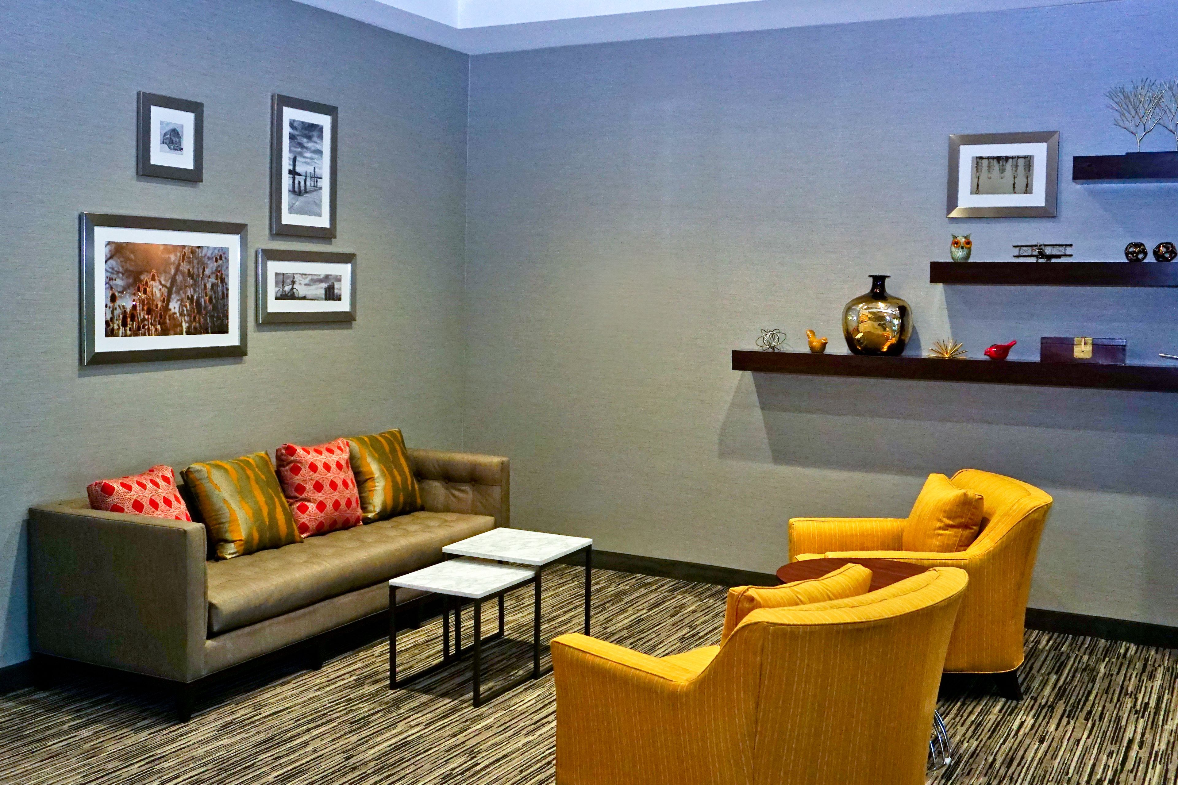 A modern living room with a sofa, two armchairs, a coffee table, and a wall decorated with framed pictures and a shelf with decorative items.