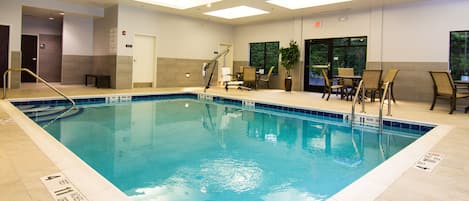 An indoor swimming pool with clear water, surrounded by lounge chairs and a seating area.