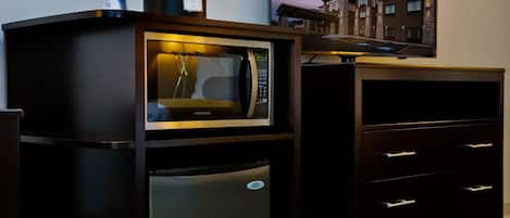 Une petite cuisine équipée d’un four à micro-ondes, d’un réfrigérateur et d’un téléviseur à écran plat fixé à un meuble.