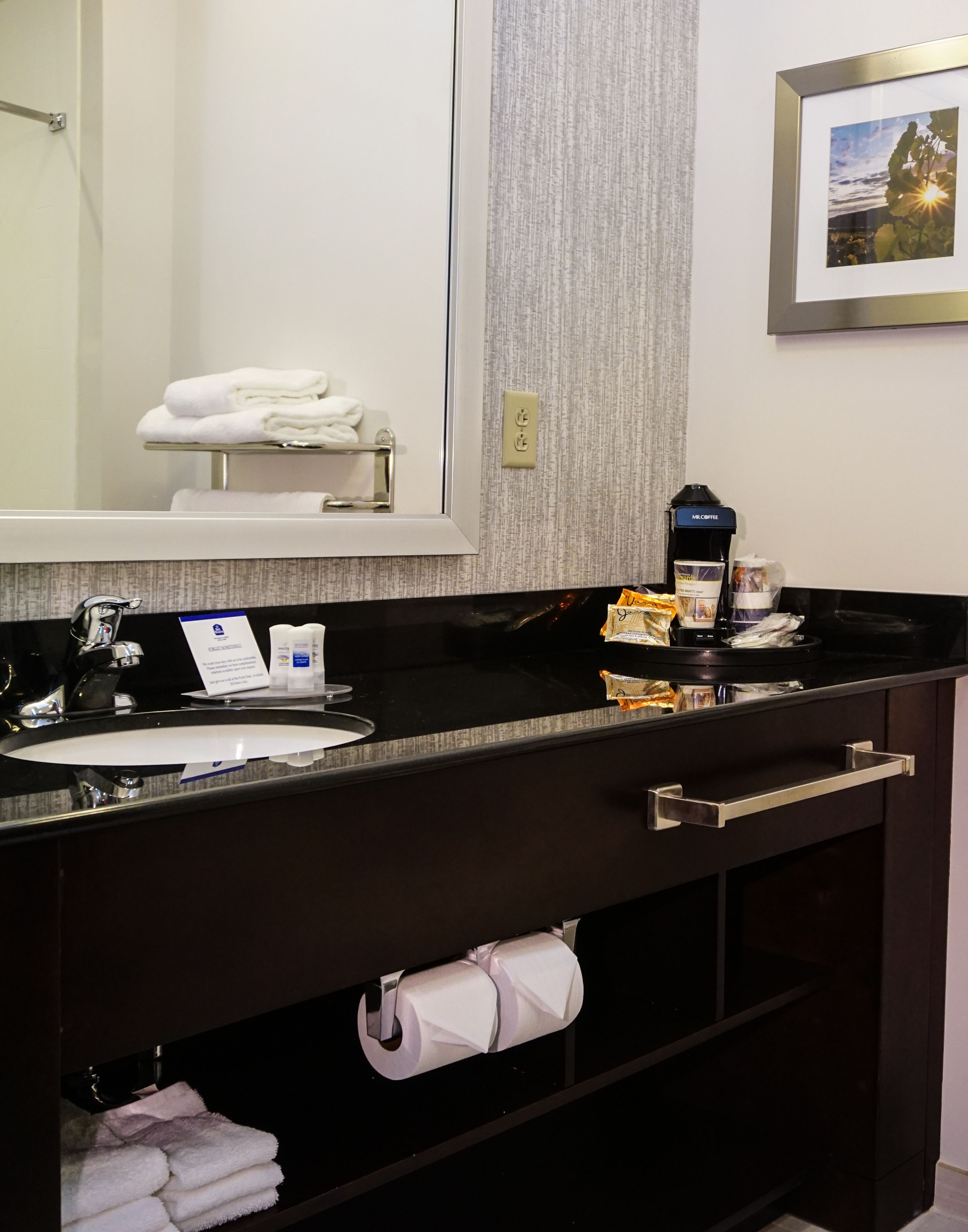 Un baño moderno con encimera negra, un lavabo, un espejo y un perchero para toallas.