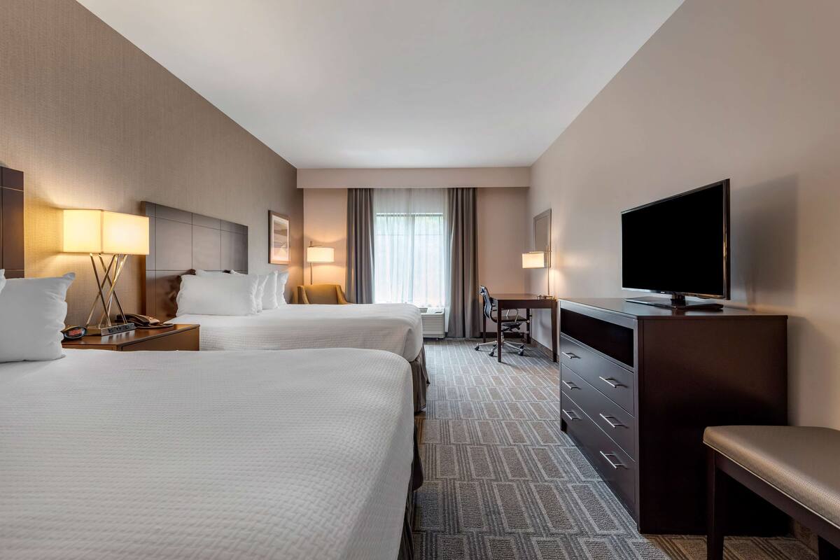 A hotel room with two beds, a desk, a TV, and a chair.