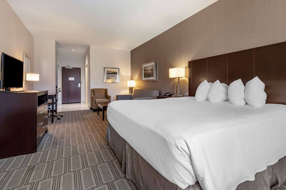 A hotel room with a large bed, a desk with a TV, a chair, and a door leading to another room.