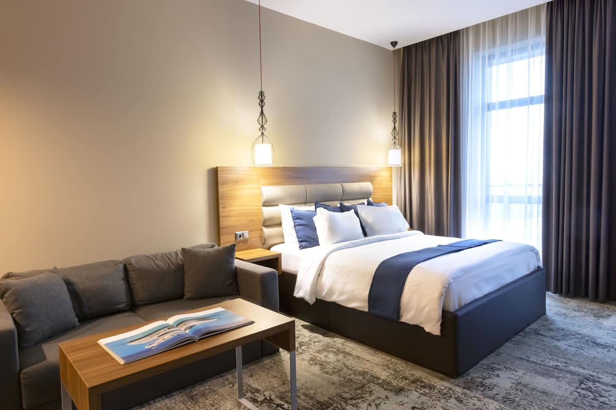 A hotel room with a large bed, a sofa, a nightstand, and a window with curtains.