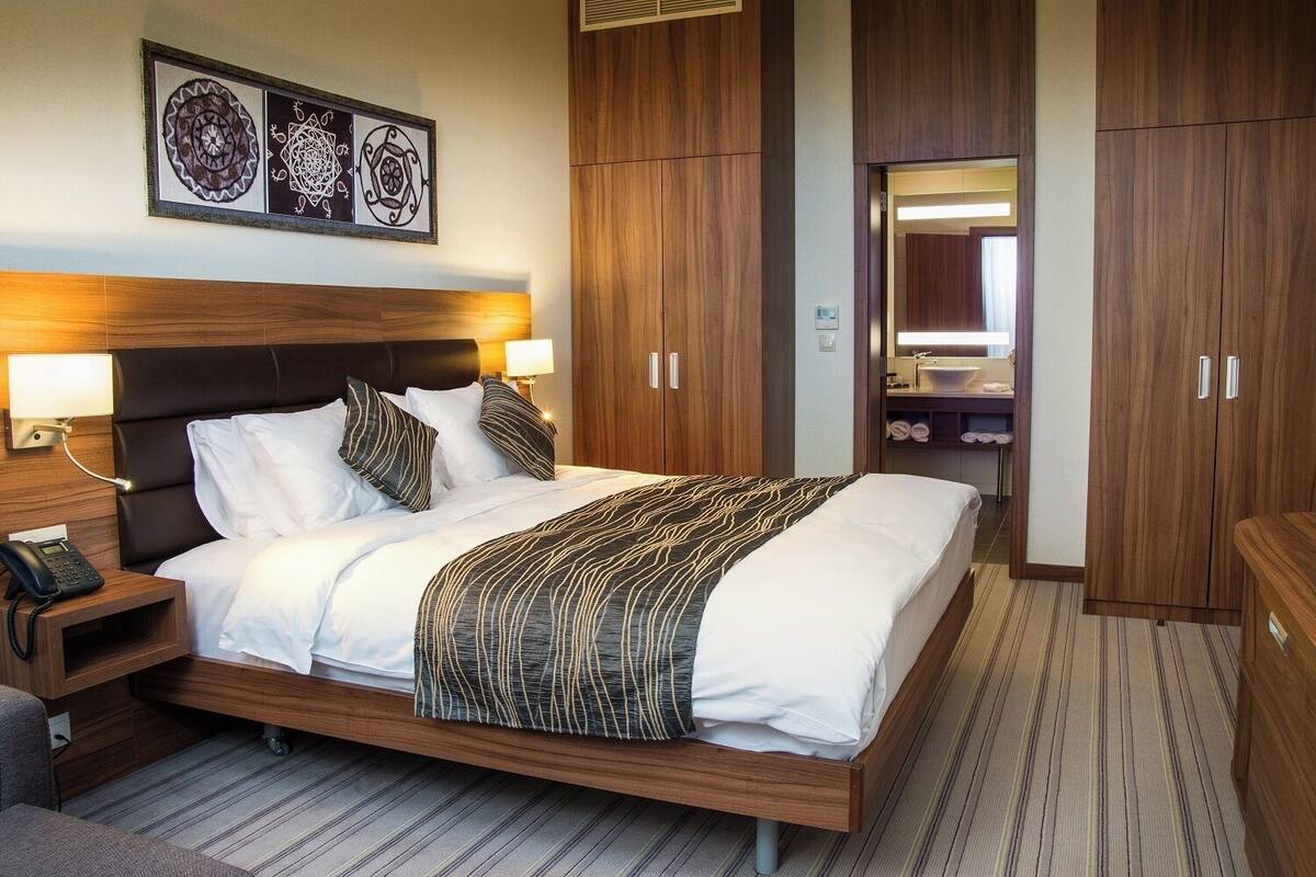 A hotel room with a large bed, wooden headboard, bedside lamps, a telephone, and a mirror.