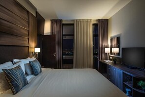 A hotel room with a large bed, two bedside lamps, a TV, and a view of the city at night. - Hotel Premier Sofia Airport (Sofia)