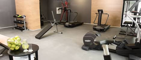 A gym with various exercise equipment, a small table with a bowl of apples and glasses, and a mirror on the wall.