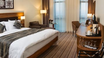 A hotel room with a large bed, a desk, a chair, and a view of the city through the window.
