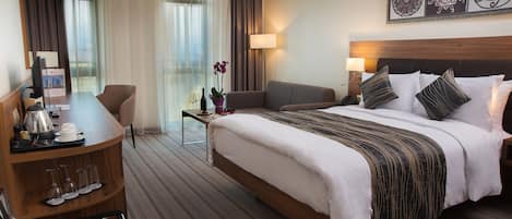 A hotel room with a bed, a desk, a chair, a small table with a lamp, and a window with curtains.