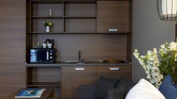 Una habitación de hotel moderna con kitchenette, un sofá, una mesita de centro y un ordenador portátil sobre la cama.
