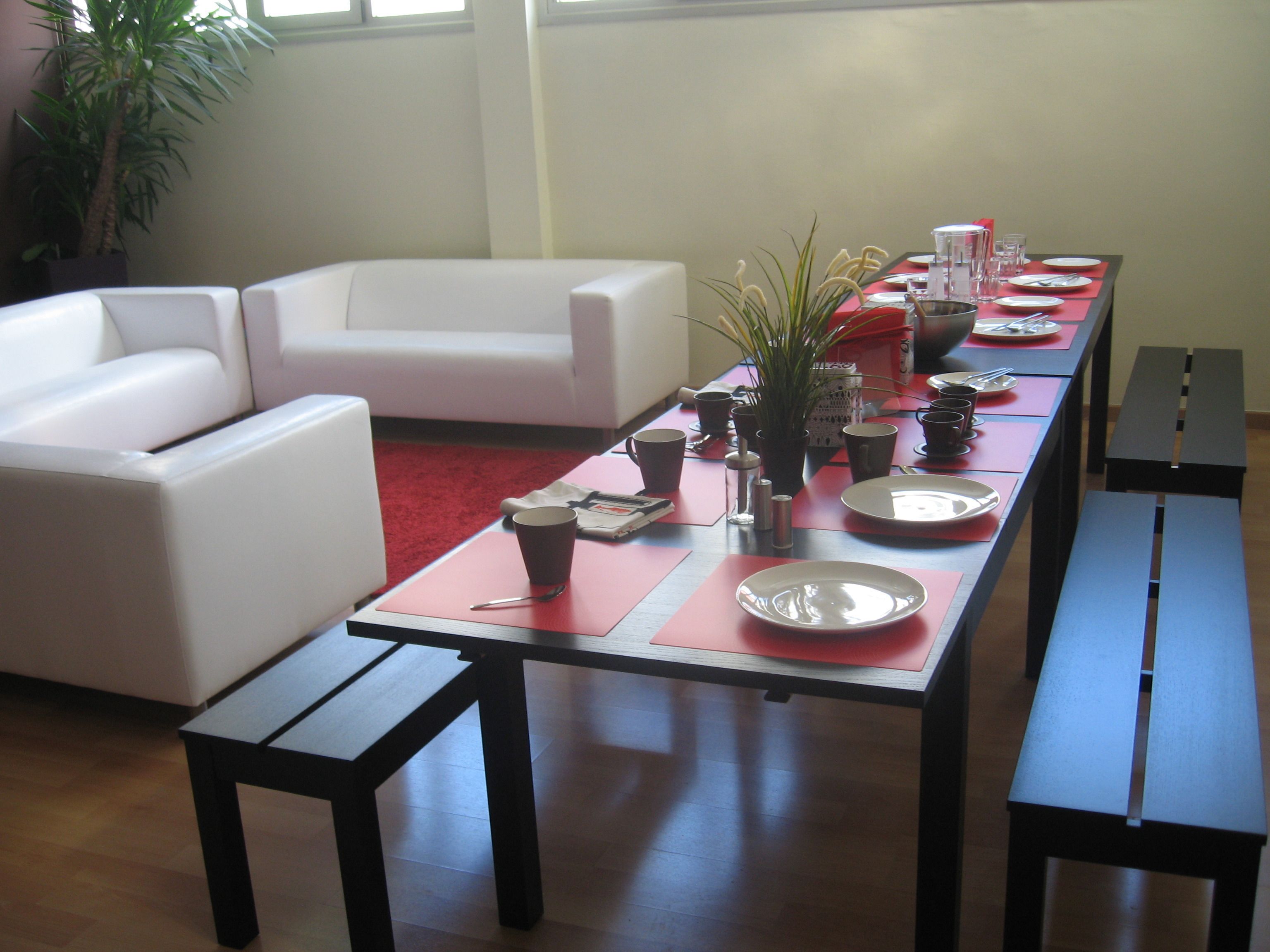A dining area with a long table set for a meal, a white sofa, and a potted plant.
