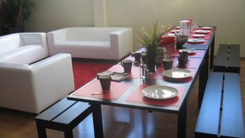 A dining area with a long table set for a meal, a white sofa, and a potted plant.