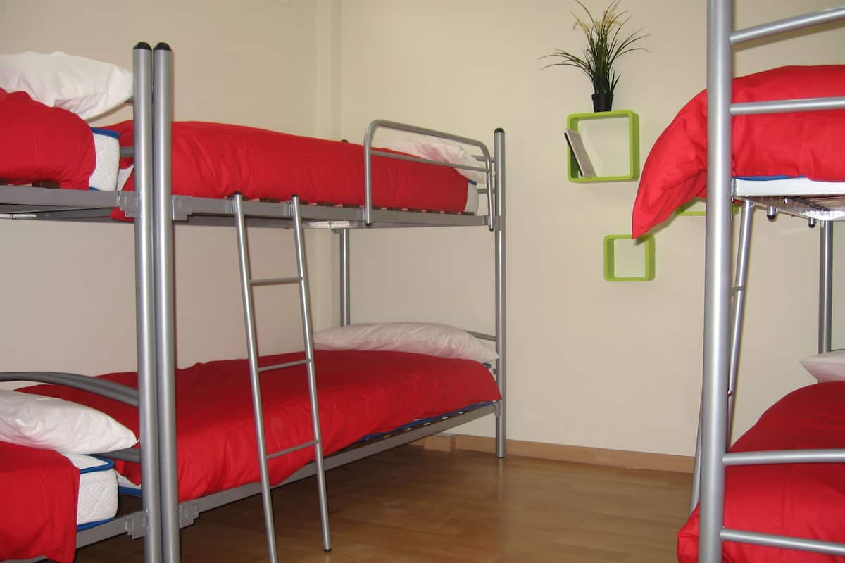 Quarto com beliches de estrutura metálica e roupa de cama vermelha.
